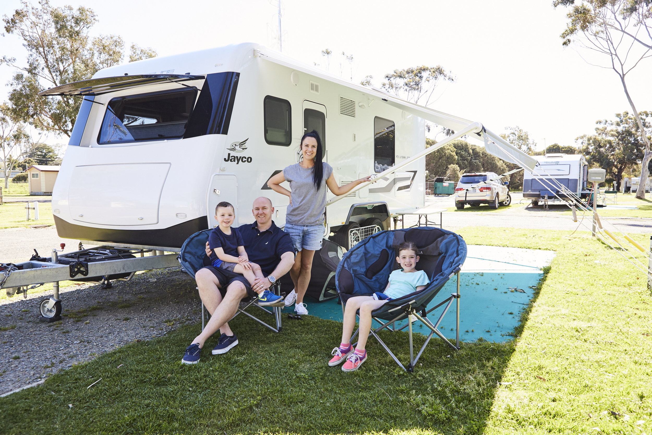 Family relaxing beside their caravan at a campsite.